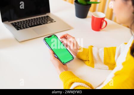Close-up unrecognizable woman in a sweater working in using a blank modern smartphone with a green screen in chroma key display sitting table office Stock Photo