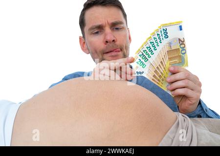 Description: An expectant father is mentally counting out future expenses for the baby and pulling out banknotes of his hand while looking at his wife Stock Photo