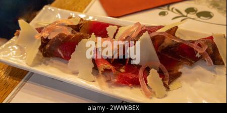 Beef carpaccio with, parmesan cheese and marinated onion in Rome, Italy. Close-up, selective focus. Stock Photo