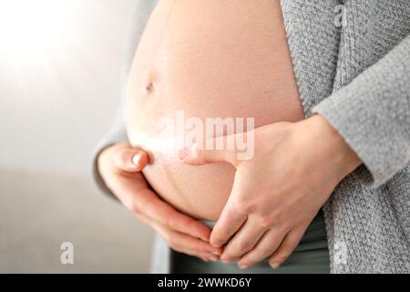 Description: Lateral view of midsection of unrecognizable woman gently holding her belly in final months of pregnancy. Pregnancy first trimester - wee Stock Photo