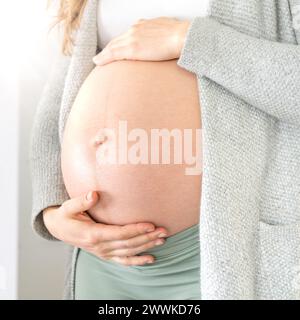 Description: Lateral view of midsection of unrecognizable woman gently holding her belly in last months of pregnancy. Pregnancy first trimester - week Stock Photo