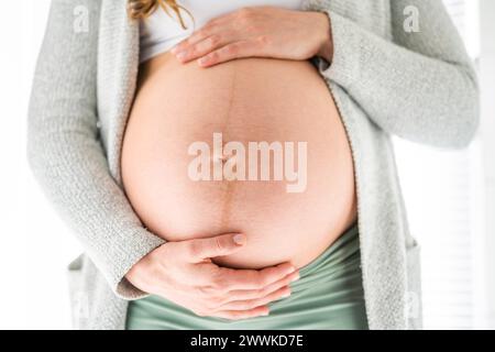 Description: Front view of midsection of unrecognizable woman gently holding her belly in final months of pregnancy. Pregnancy first trimester - week Stock Photo