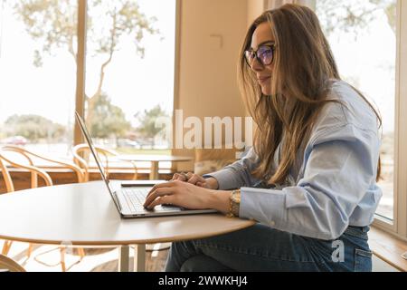 Corporate woman in light blue shirt and glasses working from her laptop smiling Stock Photo
