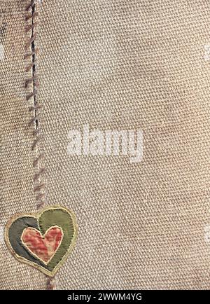 Two pieces of old burlap sewn together with thread and fabric heart. Vertical background with rustic bag texture and Valentine's day decor in patchwor Stock Photo