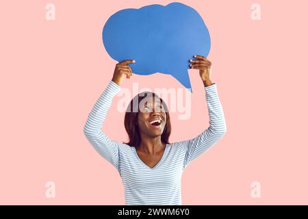 Happy young african american woman holding blank speech bubble for thoughts on pink background. Stock Photo