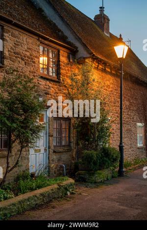 Stone cottage lit up by a street light at dusk.  Kings Sutton, Northamptonshire, England Stock Photo