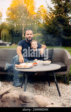 A man sitting on a black couch with his son in the backyard Stock Photo