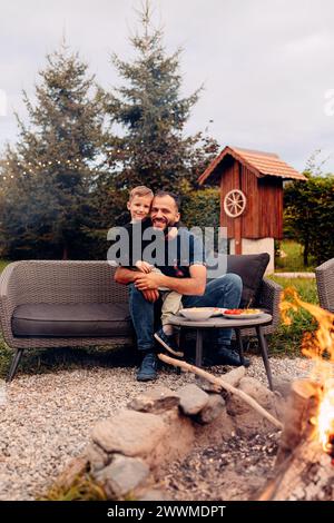A man sitting on a black couch with his son in the backyard Stock Photo