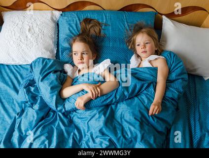 Two small smiling cute sisters are lying in bed, top view. Stock Photo