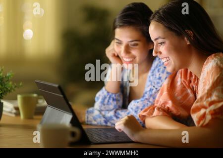 Two happy friends in the night watching videos on tablet at home Stock Photo