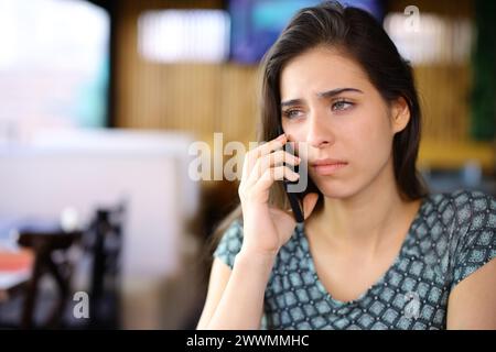Sad woman talking on phone in a bar interior Stock Photo