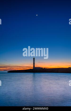 Artrutx Lighthouse in a winter twilight at Cap d'Artrutx cape with the crescent Moon conjunct Jupiter (Menorca, Balearic Islands, Spain) Stock Photo