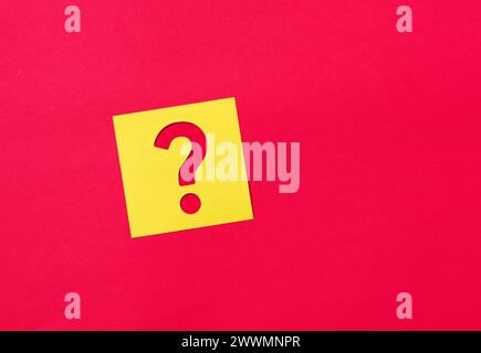 Question mark symbol on a yellow sticky note paper on red background. Stock Photo
