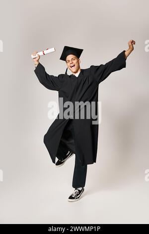 cheerful student in graduate outfit happy to have completed his studies against grey background Stock Photo