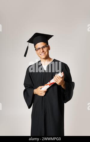 confident student in graduate outfit with vision glasses smiling with diploma in hands Stock Photo