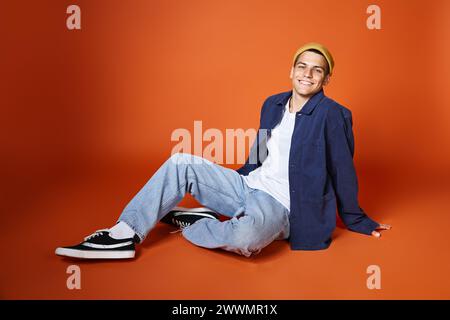 smiling man in his 20s relaxed sitting leaning on hands with backpack against terracotta background Stock Photo