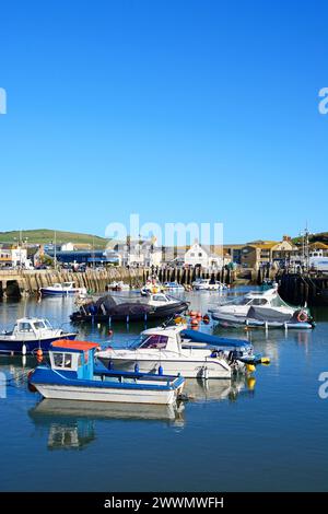 View of traditional fishing boats moored in the harbour at low tide with the town and countryside to the rear, West Bay, Dorset, UK, Europe. Stock Photo