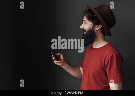 Stylish man in hat using smartphone on moody background Stock Photo