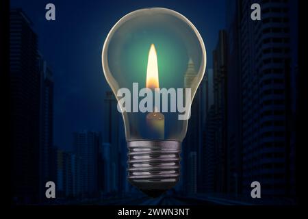 Light bulb with candle burning inside against a modern city district without electricity at night. Emergency blackout concept. Stock Photo