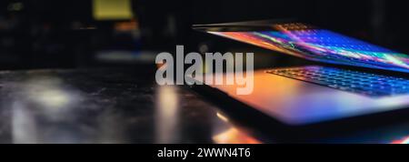 A laptop half closed in the dark with colorful glow. Stock Photo