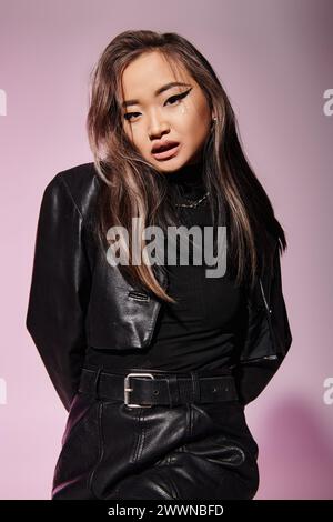 pretty asian woman in black leather outfit with heavy makeup look to camera on lilac background Stock Photo