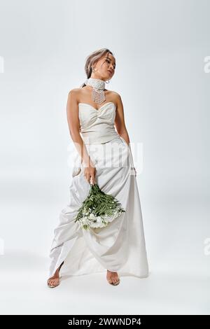 attractive young bride in white elegant outfit turning head and posing with flowers bouquet Stock Photo