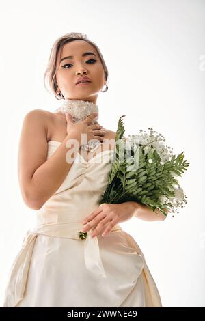 alluring asian young bride in white necklace looking to camera with bouquet of flowers Stock Photo