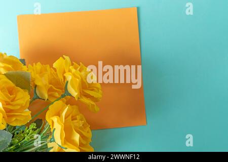 Bouquet of yellow roses with orange sheet of paper on blue background with copy space. Stock Photo