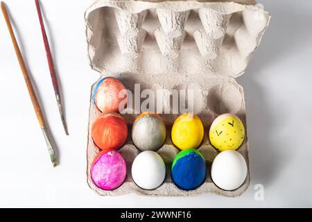 Easter eggs in a cardboard box and paint brushes on a white background, top view Stock Photo