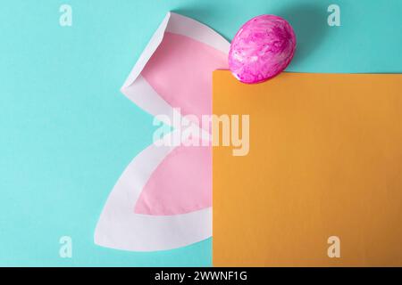Easter greeting card with rabbit ears and yellow egg on blue background, space for text Stock Photo