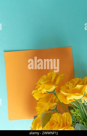Yellow roses on blue background with orange sheet of blank paper. Copy space Stock Photo