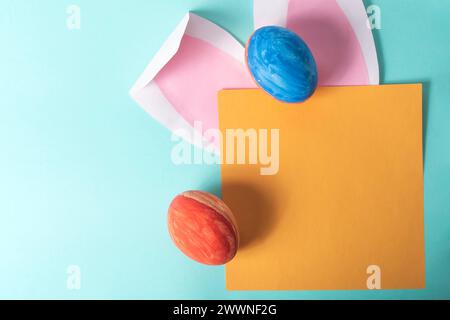 Easter eggs and blank paper card with space for text on blue background. Minimal concept, Top view. Stock Photo