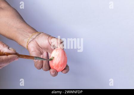 Hand of an indian woman holding an Easter egg and painting with a paintbrush on a white background Stock Photo