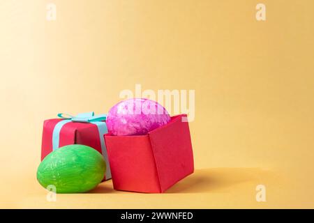 Colorful easter eggs in red gift box on yellow background. Copy space. Stock Photo