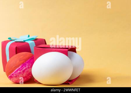 Colorful easter eggs in red gift box on yellow background. Copy space. Stock Photo