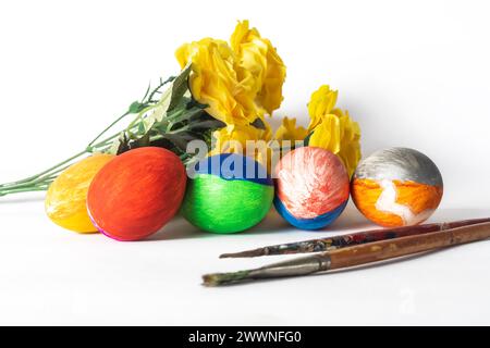 Colorful painted easter eggs with paint brushes and yellow flowers on a white background. Easter concept. Stock Photo
