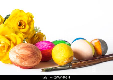 Colorful easter eggs with paint brushes and yellow flowers on a white background. Easter concept. Stock Photo