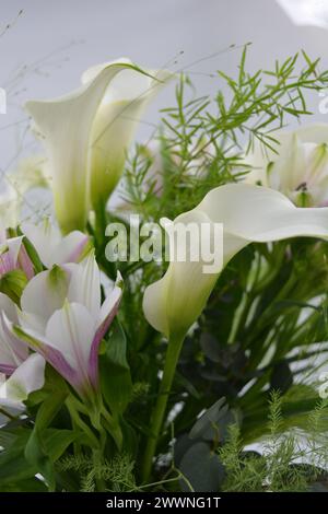 A beautiful, festive and bright bouquet, a composition of white calla lilies, purple white orchids, flowers with green leaves, branches. Stock Photo