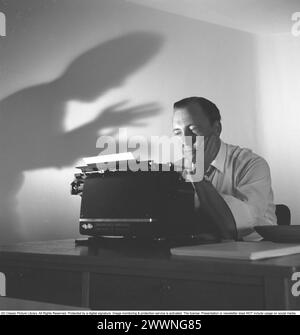 An author at his typewriter 1953. Folke Mellvig, 1913-1994, was famous for his detective novels.  For this reason the arrangement of a threatening shadow on the wall is made to enhance the fact. 1953 Stock Photo