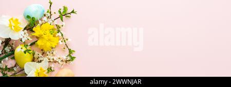 Festive banner with spring flowers and naturally colored eggs, white daffodils and cherry blossom branches on a pink pastel background Stock Photo