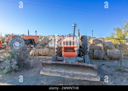 Rural farm landscape with tractors and rolled hay bales stacked behind one of the tractors. Stock Photo