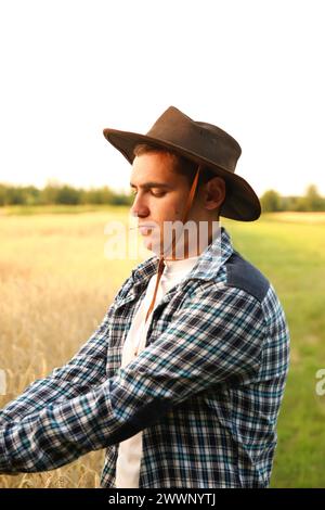 A cheerful portrait of a young cowboy-farmer. Vertical. Profile. expertise and dedication to agriculture, with a blurred agricultural landscape in the Stock Photo