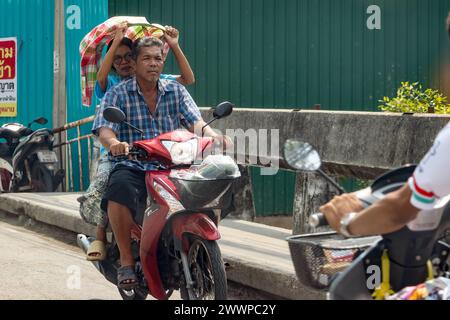 SAMUT PRAKAN, THAILAND, FEB 26 2024, A woman protects her head from the sun while riding a motorcycle Stock Photo