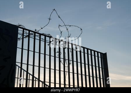silhouette of a fence with barbed wire against the light, symbol of borders, closures, imprisonments, imprisonments, and dramatic moments in the histo Stock Photo