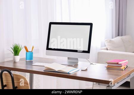 Stylish workplace with computer, books and houseplant on wooden table in room Stock Photo
