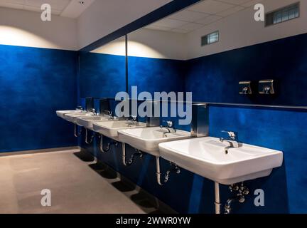 Six wash-basins in a modern blue restroom with large mirrors Stock Photo