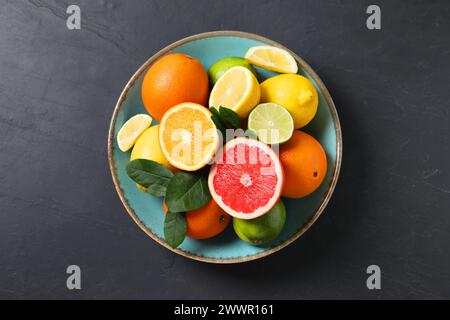 Different cut and whole citrus fruits on black table, top view Stock Photo