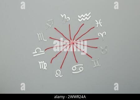 Zodiac compatibility. Signs and red threads on grey background, flat lay Stock Photo