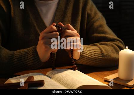 Woman praying at table with burning candle and Bible, closeup Stock Photo