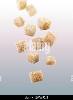Brown cane sugar cubes falling on grey gradient background Stock Photo